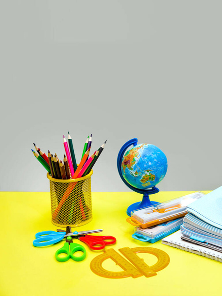 Material escolar y papelería, escritorio, globo, lápices, bolígrafos, cuadernos en la mesa amarilla
. - Foto, Imagen