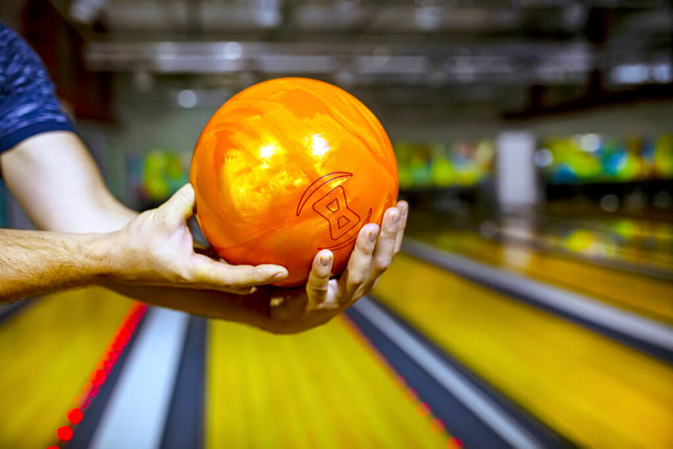 Bowling μπάλα πορτοκαλί στο χέρι του ανθρώπου φόντο μπόουλινγκ σοκάκι - Φωτογραφία, εικόνα
