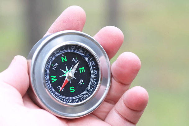 Oude klassieke navigatie kompas in de hand op natuurlijke achtergrond als symbool van het toerisme met kompas, reizen met kompas en outdoor activiteiten met kompas - Foto, afbeelding