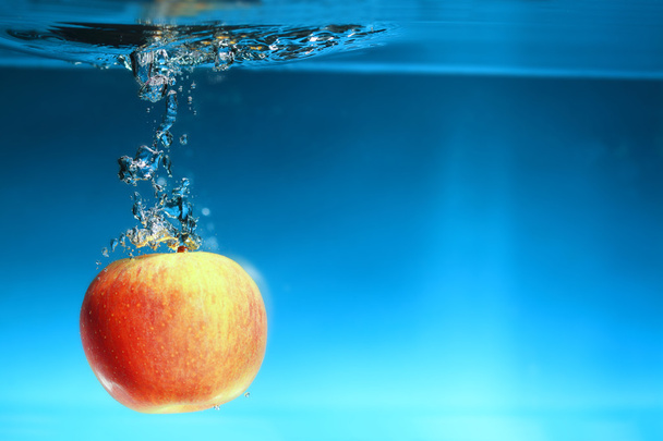 Yellow apple in the water splash over blue - Фото, зображення