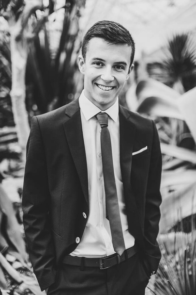 Happy handsome groom in a suit and tie is standing on the background of cactus. Man stands in the Botanical Garden. Black and white photo. - Foto, Imagen