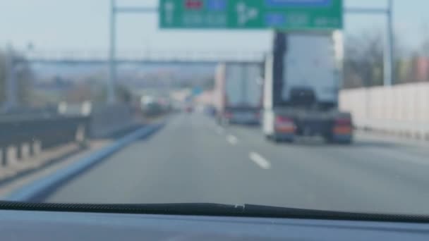 Vůz projíždí kolem a zatáčí doprava k výjezdu z rampy dálnice v Evropě, rozmazané nákladní automobily a automobily na silnici v předním okně, ruční střelba uvnitř auta. Řidičské auto na rušné silnici s nerozpoznatelnými směrovými značkami - Záběry, video