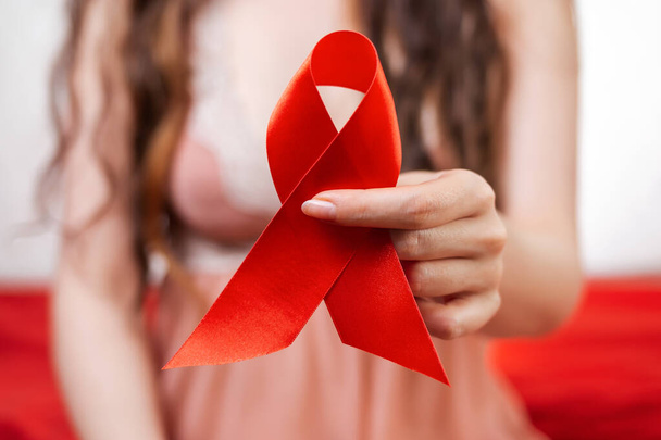 Szexuális egészség világnapja. Egy fehérneműs nő ül egy vörös ágyon, piros szalaggal a kezében. Közelről. A fogamzásgátlás és az AIDS elleni védelem fogalma. - Fotó, kép