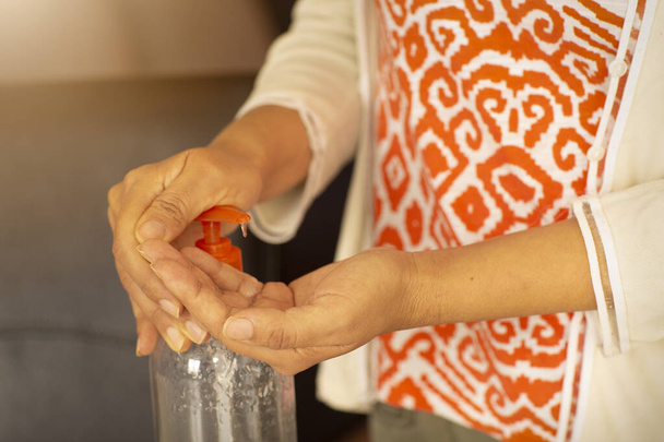 Femme avec des vêtements colorés en utilisant un gel antibactérien avec de l'alcool à la maison, nettoyage des mains, protection contre les maladies de la cornée - Photo, image