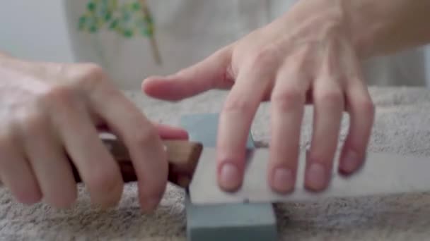 Die Hand des weißen Mannes schärft ein Küchenmesser auf einem rechteckigen Stein auf weißem Hintergrund - Filmmaterial, Video