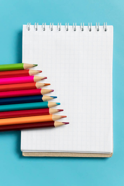 colored pencils and notebook on a blue background. Place for text, back to school. mockup, vertical - Фото, изображение