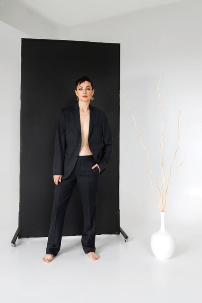 Een vrouw van 35 jaar in een zwart mannenpak op een zwart-wit achtergrond in de studio. Minimalisme - Foto, afbeelding
