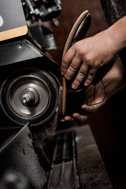 Male shoemaker repairing heel of shoe on grinding machine. Cobbler at work.  - Photo, Image