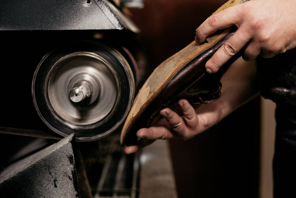 Mannelijke schoenmaker repareert schoenzool op slijpmachine. Kruimelaar aan het werk.  - Foto, afbeelding