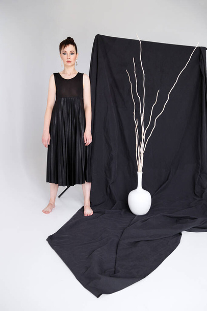 kobieta w czarnej sukience w pobliżu tkaniny czarne tło. Minimalizm - Zdjęcie, obraz