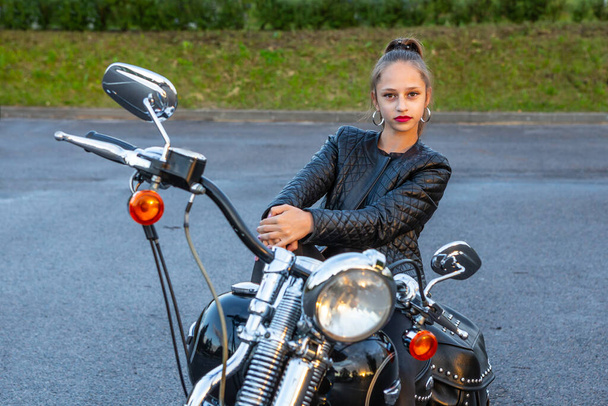 Kobieta w czarnej skórzanej kurtce rowerowej i dżinsach na motocyklu śmigłowca w mieście. Portret z bliska. Widok krajobrazu. - Zdjęcie, obraz