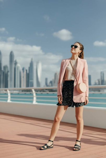 Beautiful girl in sunglasses stands against the background of the metropolis and smiles. Photo in pink and blue tones. - Foto, afbeelding