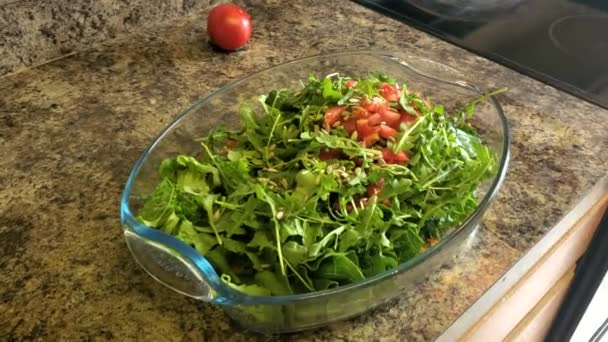 Close-up beelden van een gezonde veganistische groene salade in een glazen kom op een aanrecht. Een vrouw is het toevoegen van een dikke saus op de top van de mix die peterselie, sla, arugula, zaden, schubben omvat. - Video