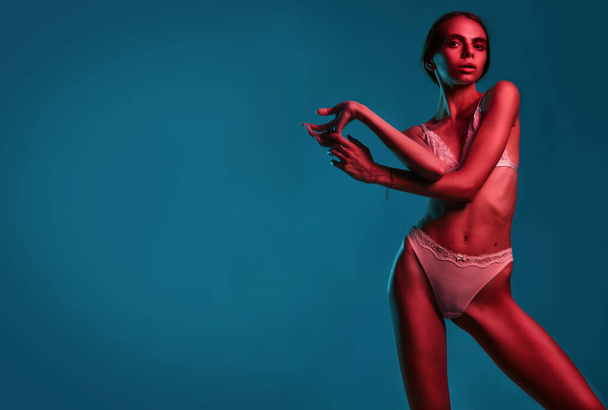 Modelo de moda magro usar lingerie erótica bege em luzes coloridas brilhantes neon uv vermelho e azul, posando em estúdio mantenha o espaço de cópia do cabelo longo - Foto, Imagem