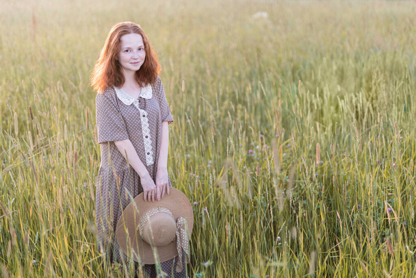redhead girl posing on a summer meadow at sunset in an elegant dress - 写真・画像