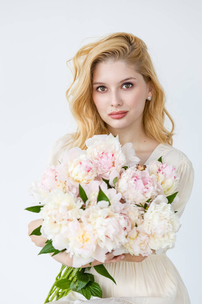 Indoor shot of beautiful girl holding white and rose peonies, winsome woman with big bouquet, enjoying her flowers - Zdjęcie, obraz