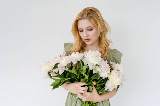 Indoor shot of beautiful girl holding white and rose peonies, winsome woman with big bouquet, enjoying her flowers - Foto, Imagem