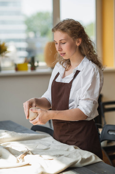 Töpferinnen formen ein Stück Ton am Tisch. Frau, die Keramik herstellt. Töpfern, handwerkliches und kreatives Geschick im Kunstatelier. - Foto, Bild