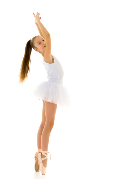 Cute little girl in a tutu and pointe shoes dancing in the studio on a white background. - Photo, image
