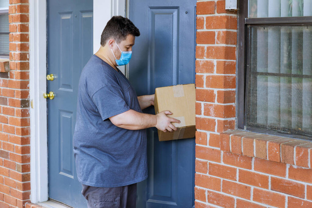 Online-Bestellung nach Hause liefern, Mann medizinische Maske mit hart arbeitenden Liefermann hält eine Box Paket der Coronavirus-Pandemie - Foto, Bild