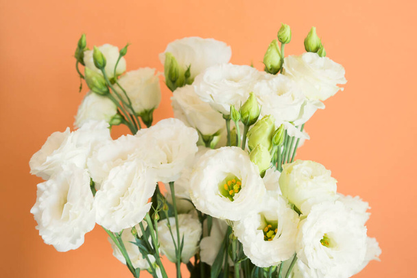 Όμορφο μπουκέτο από λευκά άνθη ευστώματος σε πορτοκαλί φόντο πεπόνι. Μοντέρνο φόντο σχεδιασμού - Φωτογραφία, εικόνα