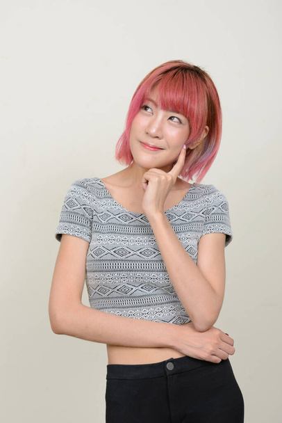 Studio shot of young beautiful Asian woman with pink hair against white background - Фото, зображення