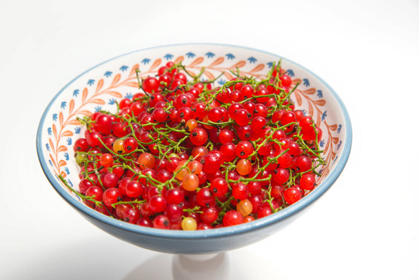 Спелые вкусные красные смородины на тарелке на белом фоне. - Фото, изображение