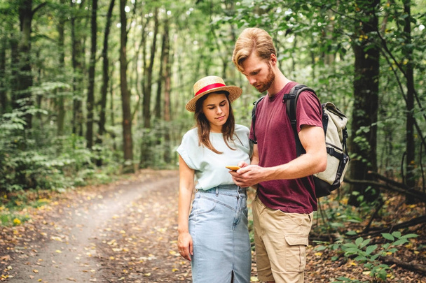 Paar wandert und nutzt Karten-App auf dem Handy. Zwei Wanderer, die auf ihr Handy schauen und versuchen, die Route zu finden. Wanderung im Wald, Smartphone suchen, Touristenattraktion suchen, Abenteuerreisekonzept. - Foto, Bild