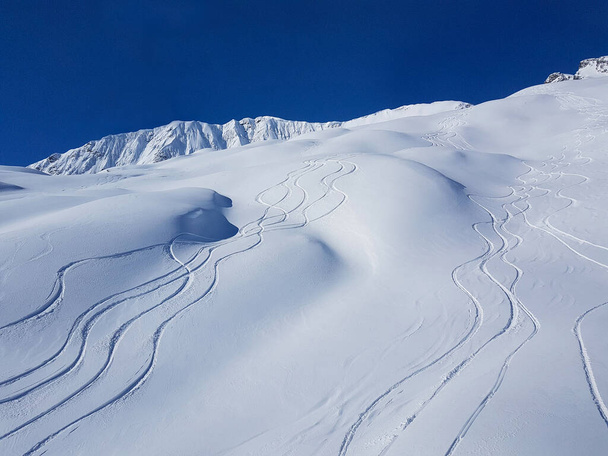 DRONE: Flying above snowboarding and ski tracks left in the deep powder snow. - Photo, Image