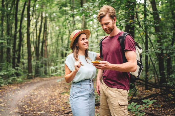 Couple using smart phone to navigate in woods. Theme tourism and navigation, search way, create route, gps phone app. Two people Hiking and Looking at Smartphone to Find the Way. - Foto, afbeelding