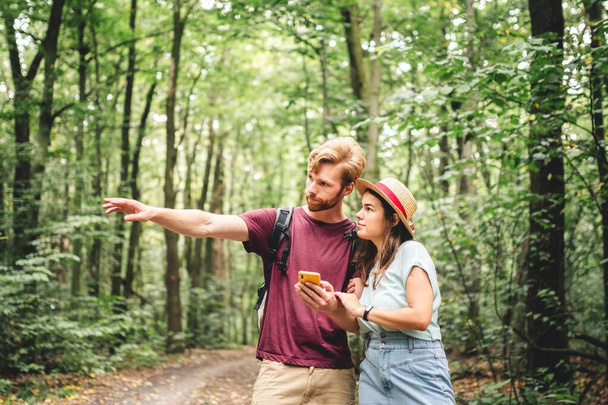 Paar wandert und nutzt Karten-App auf dem Handy. Zwei Wanderer, die auf ihr Handy schauen und versuchen, die Route zu finden. Wanderung im Wald, Smartphone suchen, Touristenattraktion suchen, Abenteuerreisekonzept. - Foto, Bild