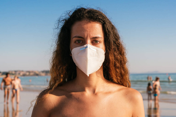 Egy fiatal lány bikiniben maszkkal. Koronavírus maszkot visel a parton. Orvosi maszkot visel nyilvános helyeken. Coronavirus karantén. Nyaralás és utazás a Covid-19 világjárványban. - Fotó, kép