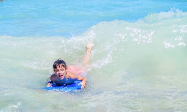Yüzünde neşe ve mutluluk ifadesi olan mavi denizde sörf yapan bir çocuk. - Fotoğraf, Görsel