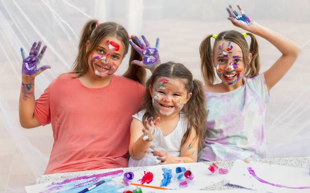 três crianças pintam com pinturas. meninas sorrir alegremente e fazer diversão. mostrar as mãos pintadas
 - Foto, Imagem