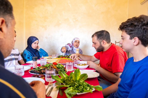 ラマダーン月のイフタールのための家族会議で一緒に食べる幸せなアラビア語のイスラム教徒の家族 - 写真・画像