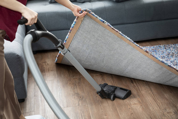 Reinigung mit einem Staubsauger unter Teppich im Wohnzimmer. Geräte zur Reinigung des Hauses. schwarzer Staubsauger. - Foto, Bild