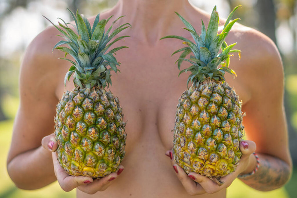 Portrait of young girl with two pineapples and palm trees around - 写真・画像