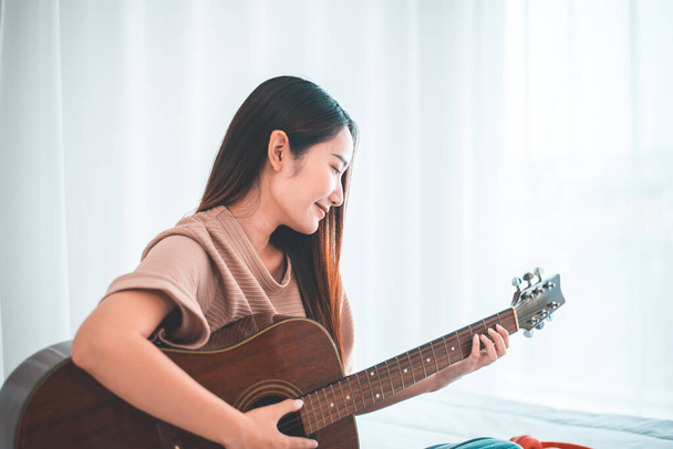 Happy young asian woman playing guitar in bedroom at home - Foto, imagen
