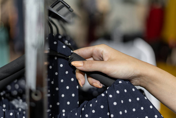 Close-up of a woman's hand takes off a dress from a hanger. Women's clothing shopping concept. - Photo, Image