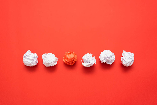 Crumpled red paper leaf ball between white balls on the red flat lay background with copy space. - Foto, afbeelding
