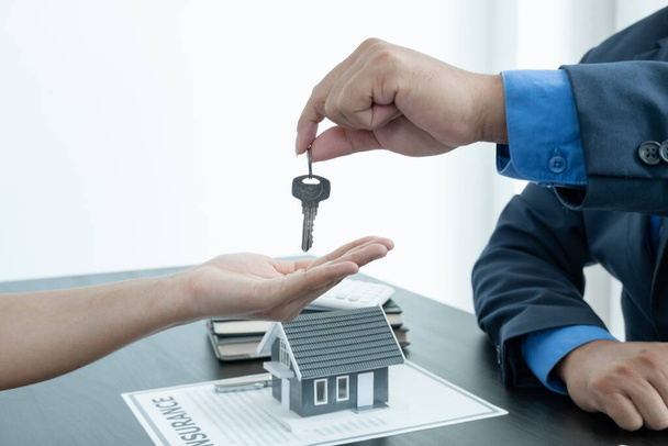 Kiinteistönvälittäjä luovuttaa talon avaimen uudelle omistajalle sen jälkeen, kun allekirjoitus on tehty sopimuksen mukaisesti vuokraamalla talo ja ostamalla talon vakuutus virallisesti päätökseen. - Valokuva, kuva