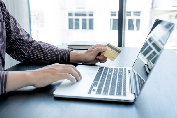 La mano del hombre de negocios sostiene una tarjeta de crédito y utiliza un ordenador portátil para compras en línea y pago por Internet en la oficina. - Foto, imagen