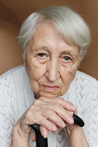Le visage et les yeux d'une vieille femme triste. Elle était assise à la maison et regardait vers la caméra. Problèmes et émotions humaines concept. Concentration sélective sur les yeux. Mains sur un fauteuil roulant - Photo, image