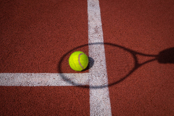Schaduwen van net en racket rond een tennisbal op een witte lijn op een buitenveld in de zon in een sport en actieve levensstijl concept - Foto, afbeelding