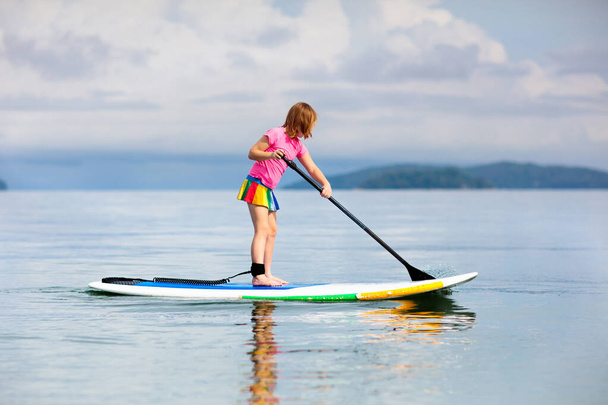 Child on stand up paddle board. Water fun and beach sport for kids. Healthy outdoor sports for summer vacation on tropical island. Holiday activity. Fit little girl training. Surfer exercising. - Photo, Image