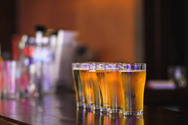 Μαλακό φως και ομαλή εστίαση, η νεαρή γυναίκα χύνεται μπύρα σε μια σειρά από ποτήρια μπύρας στον πάγκο μπαρ για να εξυπηρετήσει τους πελάτες που γιόρταζαν την επιτυχία. Η ιδέα της κατανάλωσης αλκοόλ ή μπύρας για να χαλαρώσετε. - Φωτογραφία, εικόνα