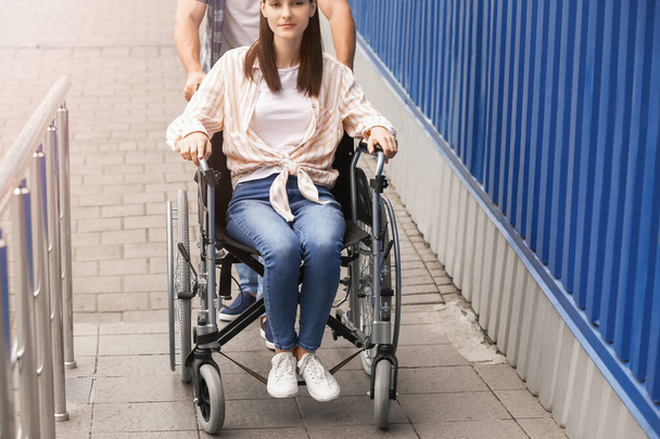Молодой человек и его жена в инвалидной коляске на рампе на открытом воздухе - Фото, изображение