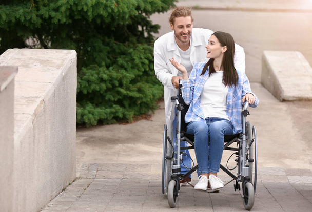 Γιατρός και νεαρή γυναίκα σε αναπηρική καρέκλα σε εξωτερικούς χώρους - Φωτογραφία, εικόνα