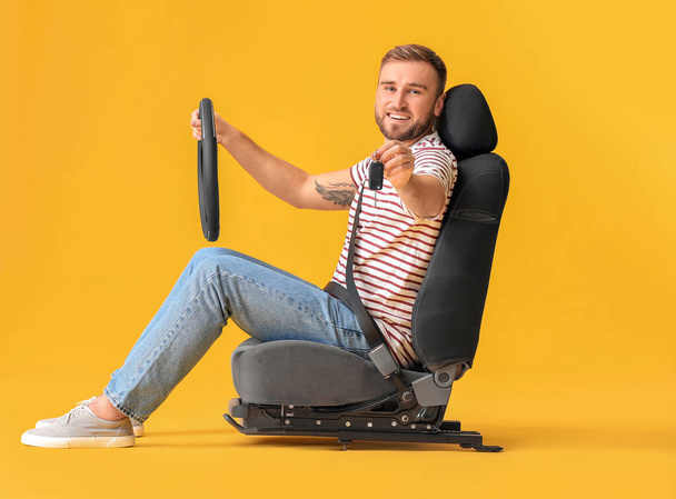 Young man with steering wheel and key sitting on car seat against color background - Fotoğraf, Görsel