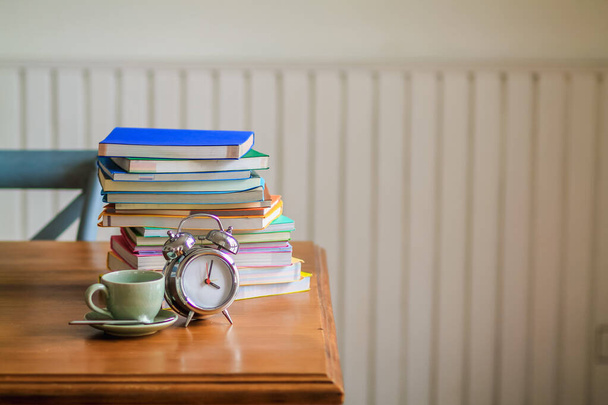 Bunte Bücher und Wecker stehen auf einem Holztisch im Haus, um sich auf den Online-Unterricht von zu Hause vorzubereiten und eine Coronavirus-Infektion zu verhindern. - Foto, Bild